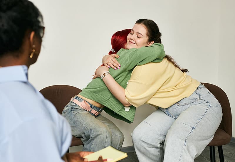 Two women share a warm hug in a bright office.