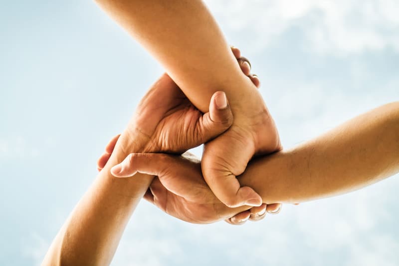 Two hands clasping each other’s wrists against a bright sky.